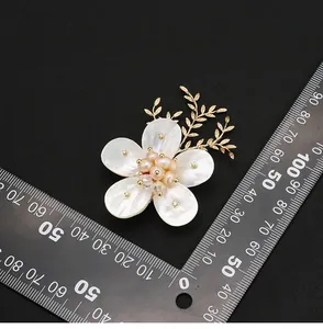 Elegante broche de flor de nácar y perlas naturales con regla para demostración