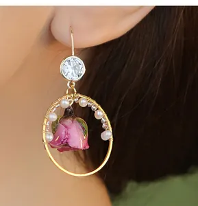 Close-up detail of gold hoop earring with natural pearls and a preserved pink rose bud