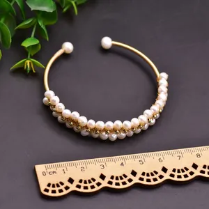 Detail of a handcrafted gold-tone bangle featuring white freshwater pearls against a dark backdrop.
