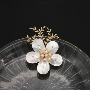 Elegante broche de flor de concha con perlas naturales y hojas doradas sobre cristal