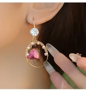 Close-up of handmade gold hoop earring with natural pearls and a real dried pink rose