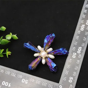 Macro view of a handmade Baroque flower brooch with pearls and blue crystals next to a ruler