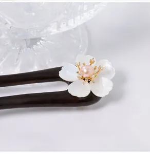 Detailopname van ebbenhouten haarspeld met schelpbloem en roze parel