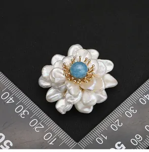 Dettaglio macro di spilla a fiore con perle d'acqua dolce e righello per misura.