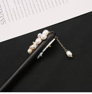 Macro view of ebony wood hair stick with natural pearl clusters and gold tassel