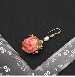 Dettaglio di un orecchino fatto a mano con rosa stabilizzata e perla su righello graduato