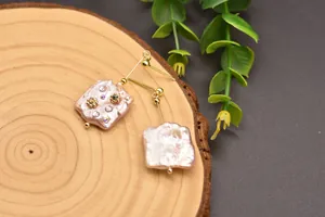 Close-up detail of irregular Baroque pearl earrings with tiny crystal floral accents.