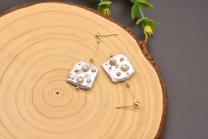 Detail of square baroque pearl drop earrings with crystal accents on a wood base