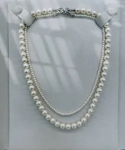 Elegant double-strand white pearl necklace with silver infinity clasp on a gray display.