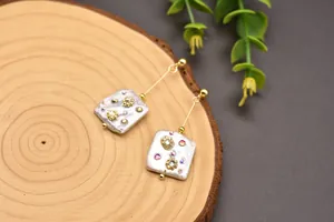 Close-up detail of square baroque pearl earrings featuring rhinestone accents on wood