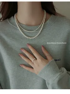 Detailed shot of a model wearing double-layered elegant white pearl necklaces on grey