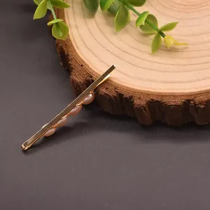 Eleganter goldener Haarclip mit natürlichen rosa Perlen auf einer Holzscheibe.