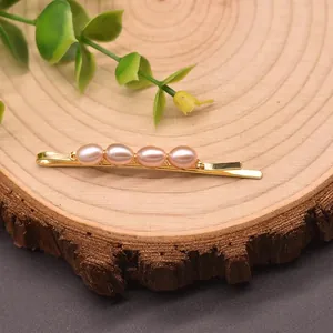 Eleganter goldener Haarschieber mit vier natürlichen rosa Perlen auf rustikalem Holz.