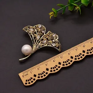 Elegante gouden ginkgoblad broche met parel en zirkoon details getoond met een liniaal