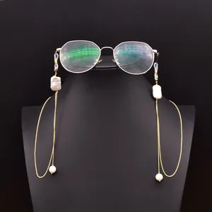 Detail view of gold eyeglass chain with baroque pearls on a black display stand
