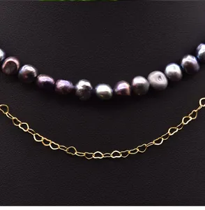 Macro detail of natural baroque pearls paired with a delicate gold heart-link chain