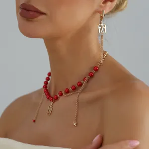 Elegantes Set aus roter Perlenkette und Ohrring mit goldenen Flügeln am Modell.