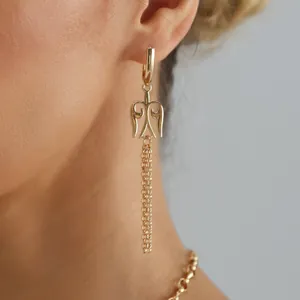 Nahaufnahme eines goldenen hohlen Flügel-Totem-Ohrrings mit elegantem Quastendetail