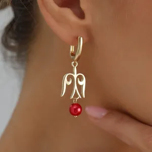 Großaufnahme eines goldenen hohlen Flügel-Ohrrings mit einer roten Perle im Detail.