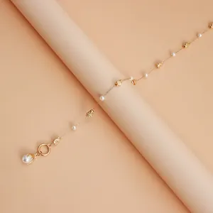 Detailed close-up of an irregular gold metal and pearl pendant necklace on a beige background