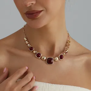 Detailed shot of a vintage geometric gold necklace with burgundy stones on a model