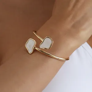 Close-up detail of a gold cuff bracelet with irregular white stone inlays on a model's wrist.