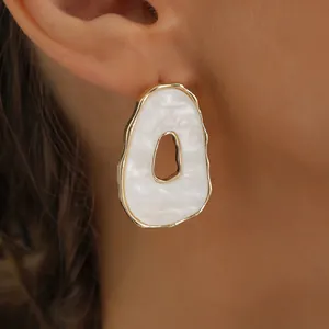 Detailed view of an irregular hollow white pendant earring featuring a gold-toned border