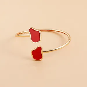Close-up detail of a minimalist gold adjustable bangle with irregular red enamel charms