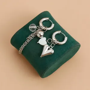 Close-up of asymmetric silver heart drop earrings on green velvet jewelry box