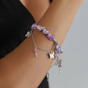 Gros plan d'un élégant bracelet en perles violettes avec des papillons argentés au poignet