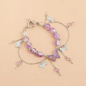 Gros plan d'un bracelet en perles violettes avec breloques papillon et pompons.