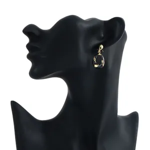 Close-up view of elegant gold and black twisted oval enamel earrings on a black mannequin.