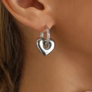 Detailansicht eines polierten silbernen Herzohrrings am Ohrläppchen eines Models.