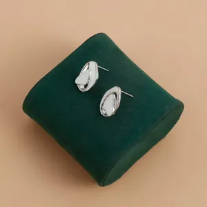Close-up of silver-toned abstract pleated stud earrings with white inlay on green velvet