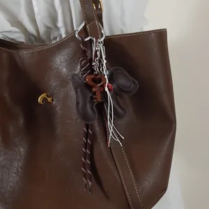 Detailed close-up of a puppy ribbon keychain and heart key charm on a brown leather bag.