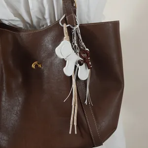 Detailed macro view of a white stylized dog charm with ribbons on a brown leather bag.