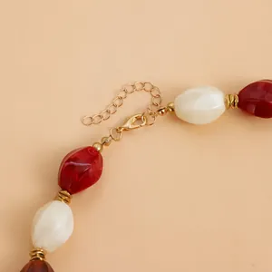 Detailed view of the gold lobster clasp and red-white acrylic beads of the necklace.