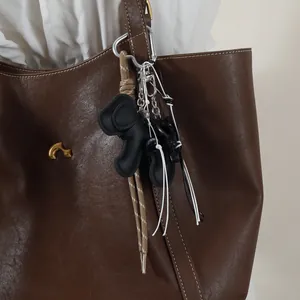 Close-up detail of a black dog-shaped woven keychain charm on a brown leather tote bag
