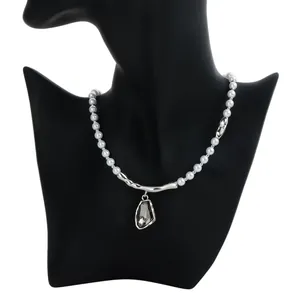 Elegante collar de perlas barrocas con colgante de gota negra sobre un busto negro.