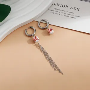 Close-up of asymmetrical hoop earrings with red floral ceramic beads and tassels.