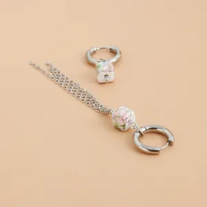 Detail shot of asymmetric silver hoop earrings with floral ceramic beads and tassels.