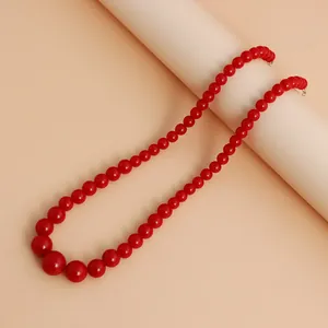 Close-up of a graduated red beaded necklace displayed on a minimalist beige background
