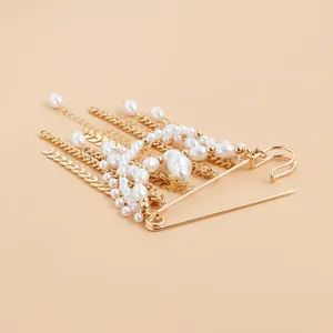 Detail shot of a gold safety pin brooch with elegant pearl and wheat chain tassels.