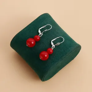 Detailed close-up view of red double bead drop earrings on a green velvet display stand