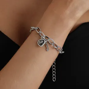 Detalle de pulsera plateada con dijes de corazón negro y llave en primer plano.