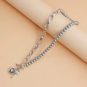 Detalle del collar de corazón y llave con cadena metálica y cuentas grises
