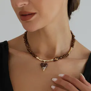 Close-up of brown beaded necklace with a golden lava heart pendant worn by a model