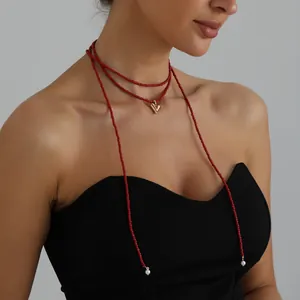 Detailed view of red seed bead necklace with gold heart pendant worn by model