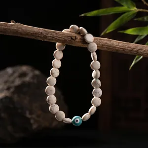 Evil eye beaded bracelet with white marble-textured beads hanging on a rustic branch
