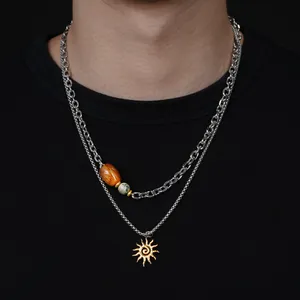 Détail d'un collier argenté à deux rangs avec un pendentif soleil et des perles décoratives.